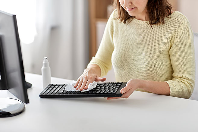 A business professional cleans and disinfects her keyboard.